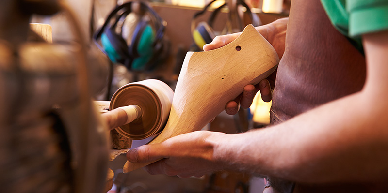 A man holds a wooden shoe last to a grinder
