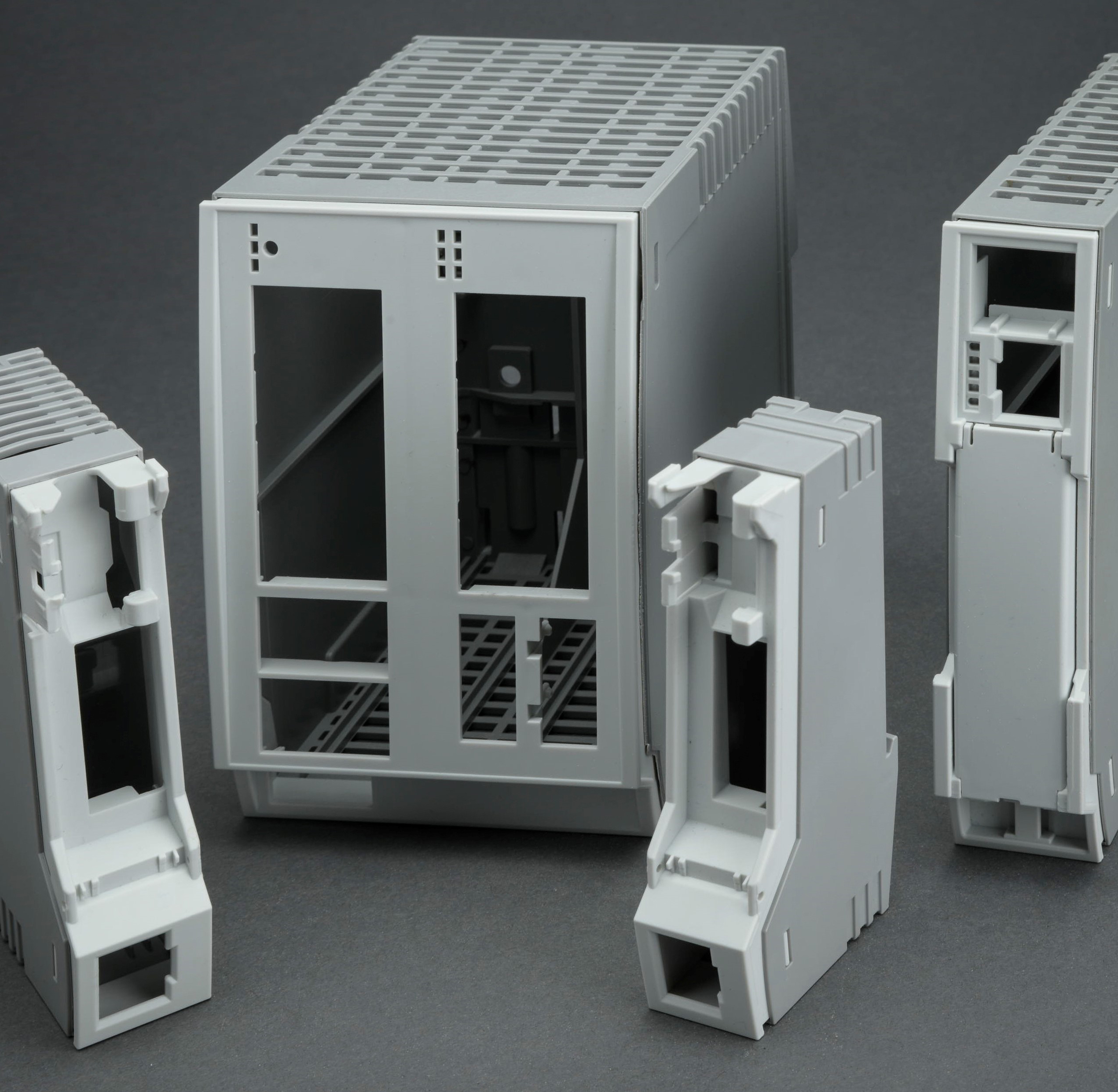 Quattro alloggiamenti prototipali in plastica grigia disposti uno accanto all’altro.